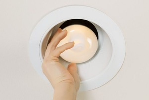 A person screwing in a bulb to a recessed lighting fixture.