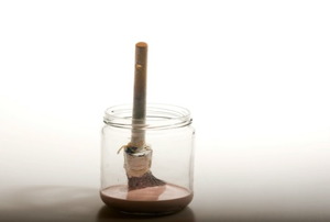 A paintbrush sitting in a glass jar filled in part with paint thinner.