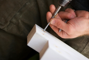 Carpenter using power tool to fix screws in door threshold.