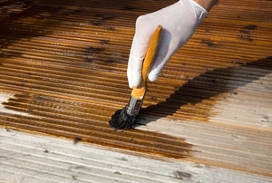 Wearing rubber gloves and applying deck stain with a brush.