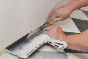 hands installing linoleum flooring against wall and cutting off excess