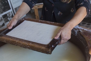 A wood tray of paper pulp held over a basin of water.