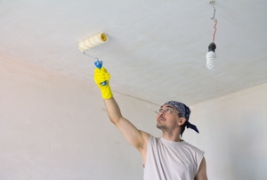 A young man in a bandana painting a ceiling white.