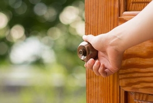A woman opens a wood exterior door.