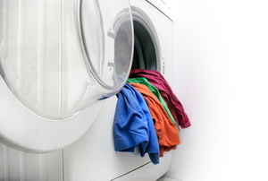 A rainbow selection of shirt hanging over the edge of a white washing machine basin.