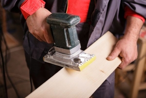 A DIYer working with a belt sander on a piece of lumber.