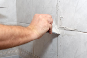 hand applying grout to tiles on a wall