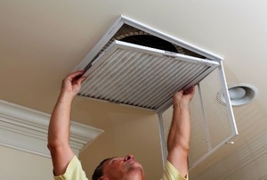 A man reaching up to open filter holder for HVAC in the ceiling.