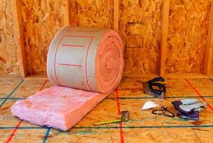 A roll of pink, fiberglass insulation and related tools in front of an unfinished wall.