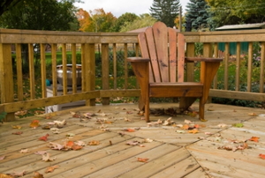 A backyard wooden deck with an adirondack chair on top.