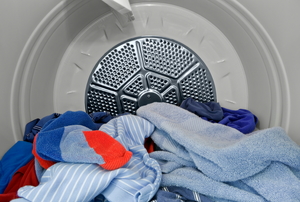 A clothes dryer with a pile of shirts inside. 