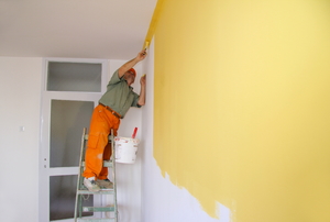 A painter covering a white wall in yellow interior paint.