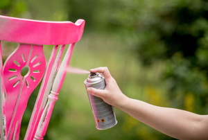 A  woman spray paints a chair.