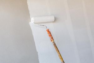 A paint roller applying white paint to a wall.