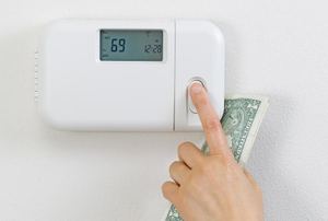 A hand adjusting a digital thermostat while holding cash.