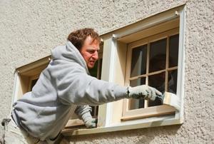 A homeowner working on window trim with a paint brush.