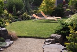 A landscaped backyard with a pair of orange lounge chairs. 