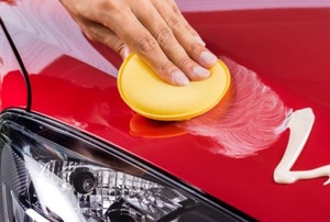 hand applying wax to red car with pad