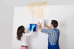 A couple using buckets to catch water leaking from the ceiling.
