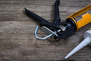 A caulk gun against a weathered wood background.