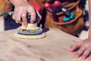 woman sanding a wooden surface with an electric power sander