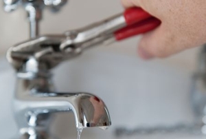 hand with wrench working on sink faucet plumbing