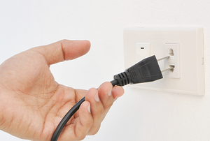 a hand unplugging a cord from an outlet
