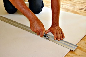 A man's hands cutting drywall with a utility knife.