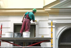 a man on a scaffold paints a white house yellow