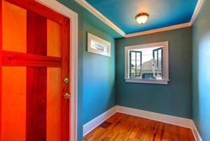 A robin's-egg-blue room with white baseboards and crown molding, as well as a wooden door and floor.