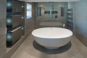 A white oval shaped bath tub in an expensive new home in an ultra modern bathroom.
