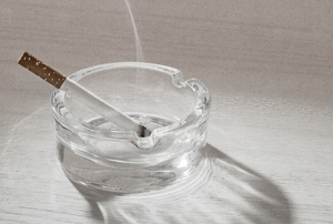 A smoking, lit cigarette in a clean glass ashtray.