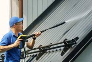 man power washing a metal roof