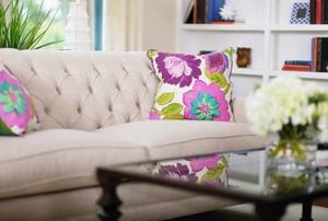 A modern living room with a cream colored couch and flowered pillows.