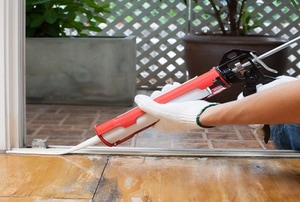 A tube of silicone caulking being used to seal the edge of a metal threshold.