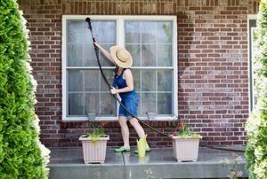 A woman cleaning windows outside her brick house. 