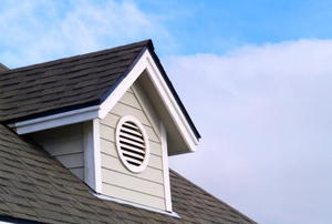 A gable vent jutting out from a roof with blue sky behind.
