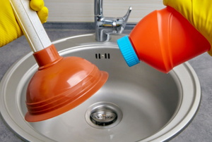 gloved hands with plunger and liquid above small metal sink