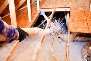 Blowing insulation into a hole in an attic floor from the viewpoint of the installer.