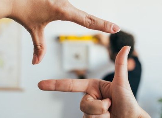 person's hands held up like a frame around another person hanging picture