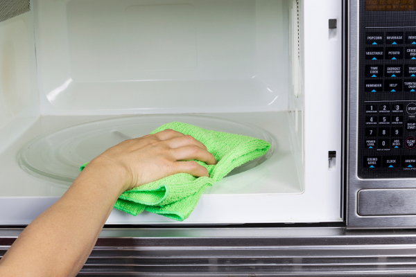 A green cleaning cloth wiping out a microwave. 