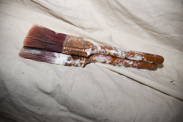 A pair of used paintbrushes on a drop cloth. 