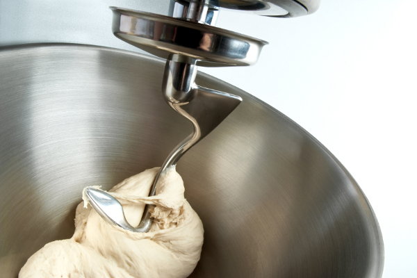 A stainless steel mixer bowl with bread dough in it. 