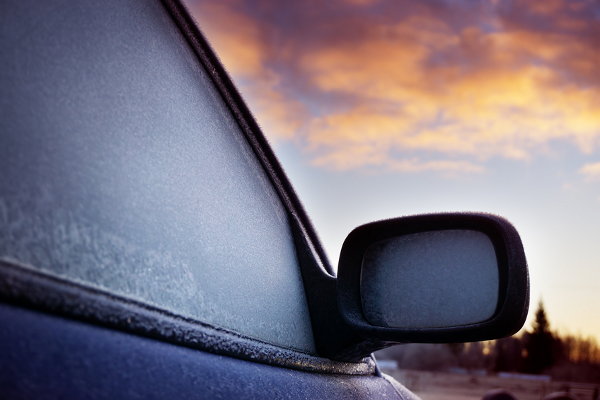 A car with frost on the window facing a sunrise. 