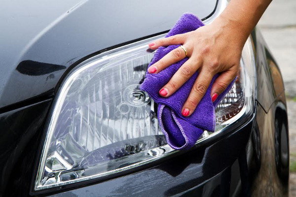 Cleaning the headlights on a car with a purple rag. 