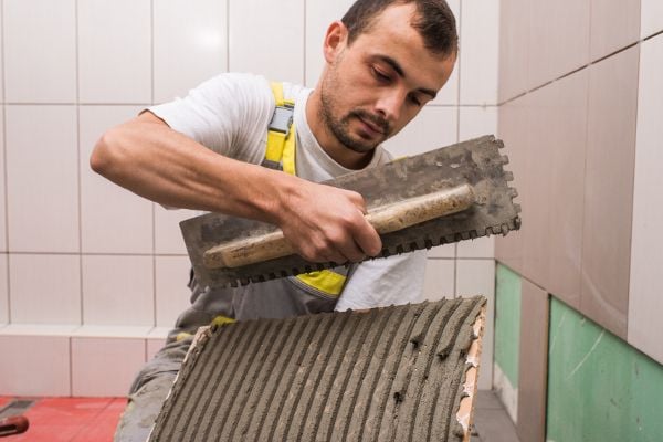 a handyman grouting tile in a bathroom. 