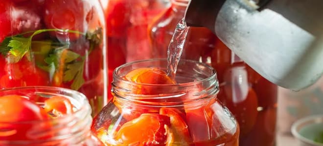 Hot water being poured into glass jars full of tomatoes. 