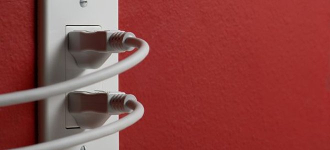 Two cords are plugged into an electrical outlet on a red wall.