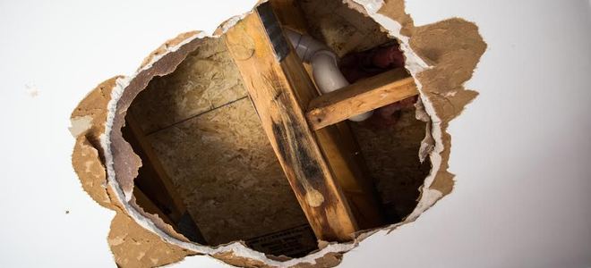 A hole in a ceiling exposing pipes and beams.