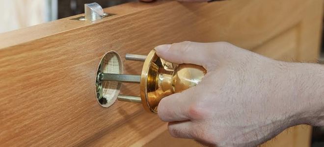 A pair of hands installing a doorknob on a door.